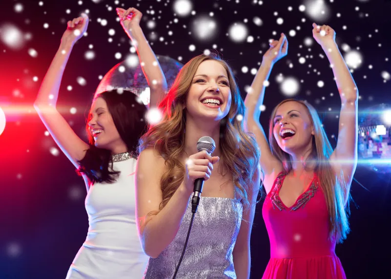 Three women singing and dancing karaoke at a company party